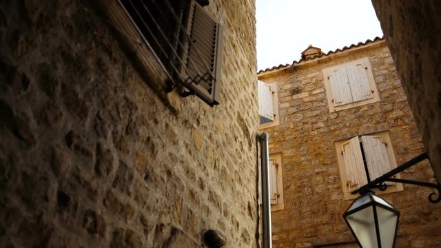 View on the alley in shadow between stone houses of Mediterranean architecture style with closed windows. Outside
