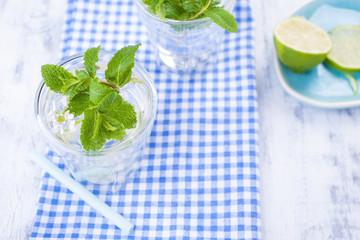 Two glasses of water and fresh green mint, and lime. On a blue napkin on a wooden background. free space for text or a postcard.