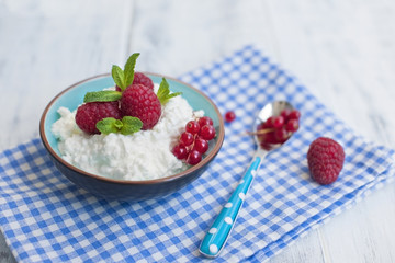 Light breakfast at home, a bowl of cottage cheese with berries of red raspberries and currants. Blue napkin and spoon. Free space for text or a postcard.