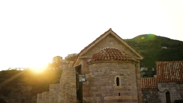 Ancient small church in Mediterranean style on the sea coast and high picturesque mountains on the background. On the sunset in the summer. Outside