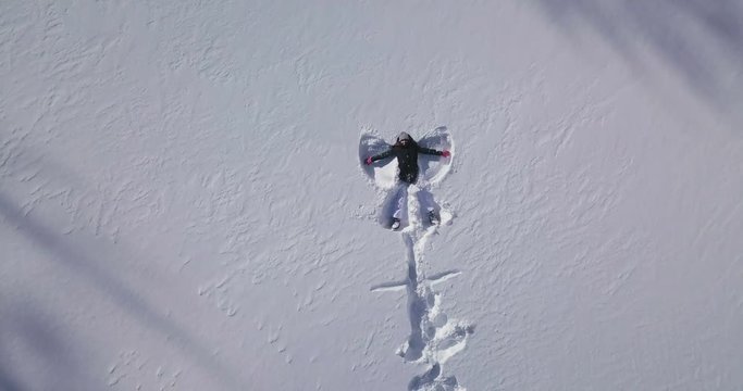 Aerial view of a woman on a holiday in the mountains having fun and playing "the snow angel" immersed in the white snow just fallen. Concept of: fun, vacation, mountain.Aerial view of a woman on a hol