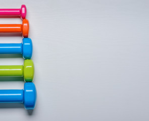 many blue green and one orange in the middle dumbbells on a white background ,concept preparing to fitness sports equipment top view mock up