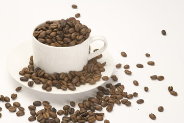 Coffee beans in a white cup and saucer on a plain background