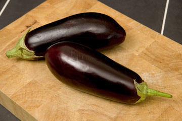 Two purple eggplant aubergines on a wooden chopping board