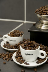 Still life of roast coffee beans, espresso cups and grinder on a tiled kitchen work surface