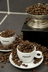 Still life of roast coffee beans, espresso cups and grinder on a tiled kitchen work surface