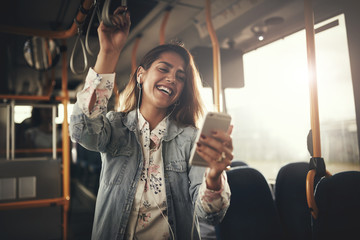 Young woman laughing while listening to music on a bus - obrazy, fototapety, plakaty