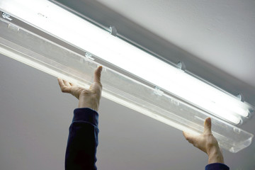 Electric hands changing ceiling fluorescent lamp. The concept of repair and service.