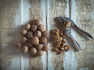 walnuts on the rough wooden surface next to the cleaned and an instrument for cracking nuts toning