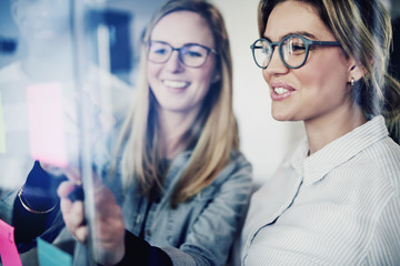 Two businesswomen brainstorming with sticky notes on a glass wall