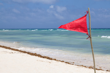 Red flag on a beach. Beautiful sea view, white sand, blue sky