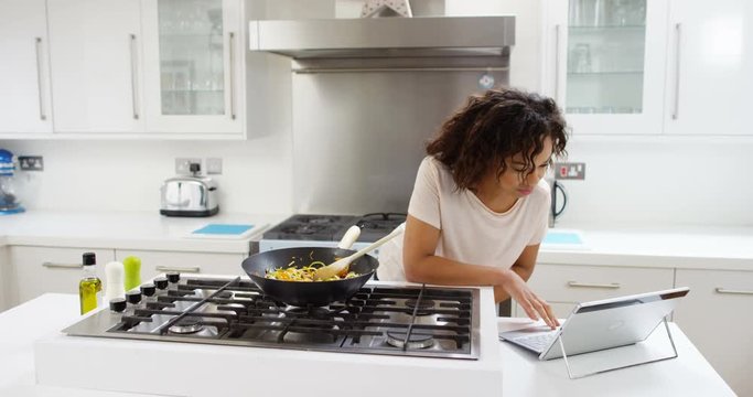 4K Woman preparing a healthy meal at home, following a recipe on computer. Slow motion.