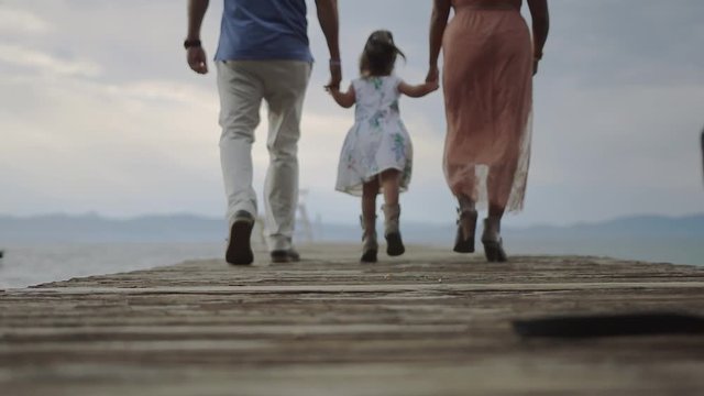 4k Family skipping along a dock, looking at their backs,