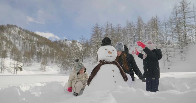 On a winter day, in the mountains with snow, a family plays the snowman together. Concept of: winter holidays, family, christmas, mountain