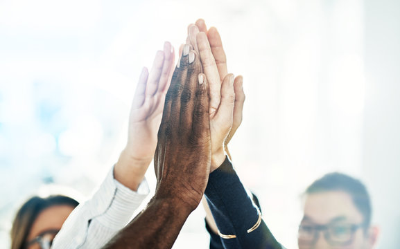 Diverse work colleagues high fiving together in an office