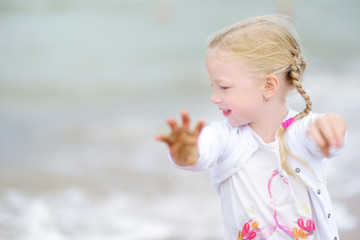 Cute little girl having fun on a sandy beach on warm and sunny summer day. Kid playing by the ocean.