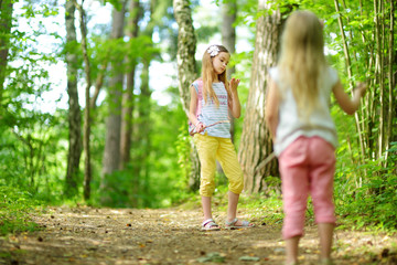 Two cute little sisters having fun during forest hike on beautiful summer day. Active family...