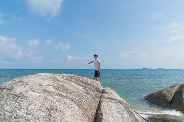 Boy standing on large rock on water's edge on Bang Kao beach Ko Samui.