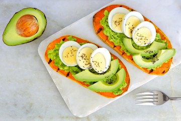 Sweet potato toasts with avocado, eggs and chia seeds on a marble server. Top view on a bright background.