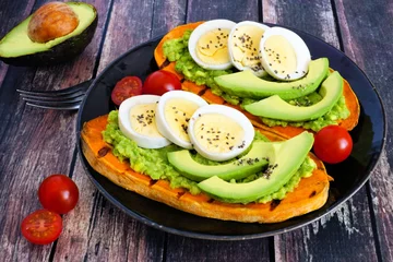 Sweet potato toasts with avocado, eggs and chia seeds on a dark plate. Table scene with a wooden background.