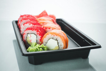 Beautiful rolls in black container on white background with reflection, for a menu or website