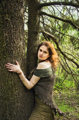 young witch hugging tree trunk in spring forest