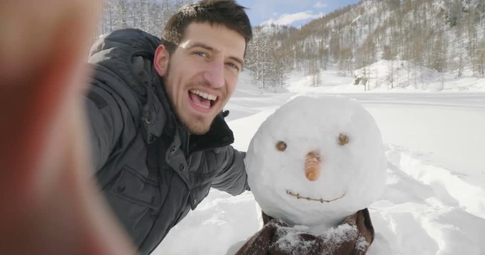 On a winter day, a man in the mountains makes a video call and greets his wife or friends on the phone. Concept of: winter holidays, technology, christmas, connection