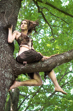 woman forest spirit sits on the branches of an old oak tree. costume and crown hand-made of felt