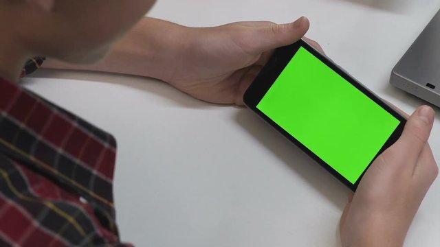 Teenager watching movie on smartphone at home table, free time, green screen