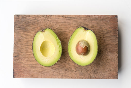 Directly above view of avocado cut in half on wooden chopping board on white table
