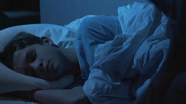 Mother gently stroking head of sleeping son, covering with duvet, family care