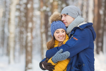 Young man hugs young girl in a forest in the winter