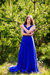 Obraz na płótnie Canvas Beautiful fashion model in a dress in a green park in the summer . Blue dress.