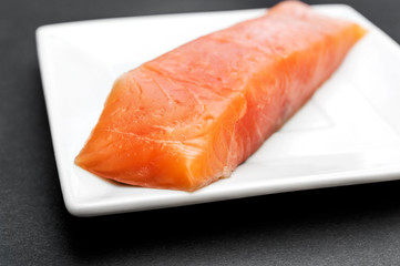 Plate with fillet of red fish on black background.
