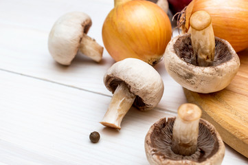 Mushrooms and onions with cutting board on the white wooden table.