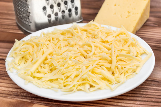Plate with grated cheese, grater and piece of cheese and on the table.