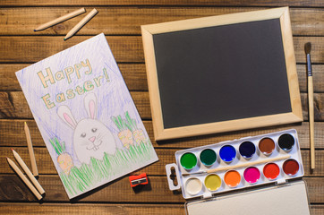 A child's drawing on the theme of Easter: egg, Bunny, congratulation with Easter. The view from the top, paints, pencils, brush and pattern. Free space for text.