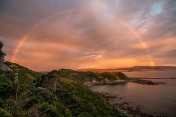 Naklejka na ściany i meble Rainbow and sunset along ocean coastline