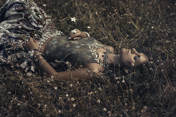beautiful young eastern girl in ethnical jewelry lying on a grass on a field