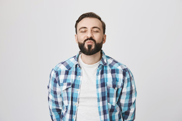 Portrait of attractive middle-aged bearded man, waiting for kiss with folded lips and excitement, closing eyes and standing over gray background. Spouse tries waits to recieve morning kiss from wife