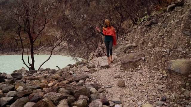 Young caucasian woman walking near Kawah Putih White Crater sulphur lake on misty day