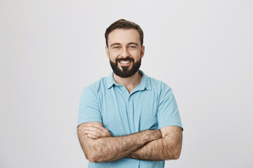 Portrait of a handsome bearded man smiling looking to the camera with his hands crossed isolated on white background. This person looks like an ordinary guy who is sincere and ready to help everyone.