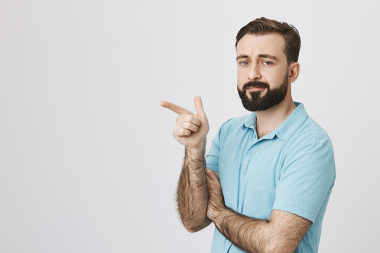 Person with a handsome beard and moustache wearing casual clothing pointing somewhere isolated on a white background. Tired consultant at store shows customer where is dressing room