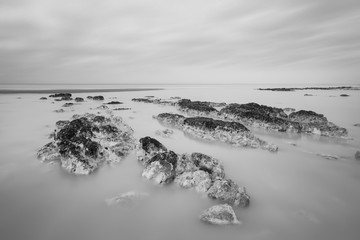 Superbe image de paysage à longue exposition en noir et blanc de la plage à marée basse avec des rochers au lever du soleil
