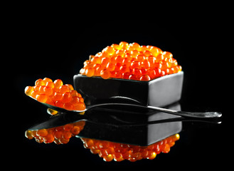 Caviar in a spoon. Salmon caviar in a bowl over black background. Closeup trout caviar
