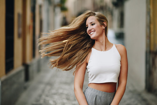 Fototapeta Happy young woman with moving hair in urban background.