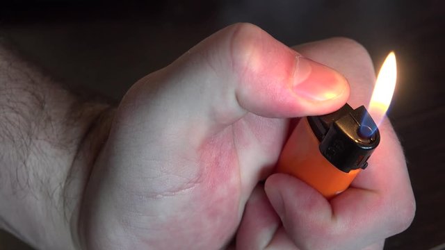 Man ignites a lighter lighting orange color lighter 4K close up view