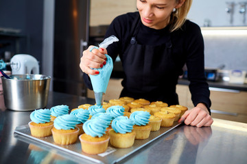 The confectioner with a pipping bag of cream in his hands decoretion cupcake on the table in the...