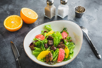 Salad with citrus, lettuce and grilled chicken liver in a plate.