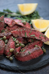 Beefsteak tagliata with chopped fresh rosemary, caper berries, olive oil and lemon, close-up, selective focus, vertical shot